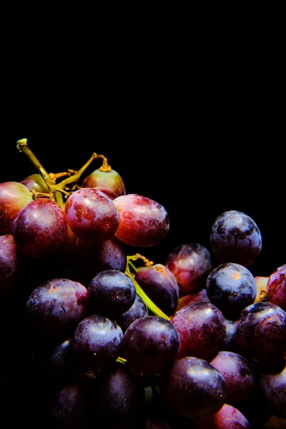 Free Photo vertical closeup of red grapes under the lights isolated on a black background