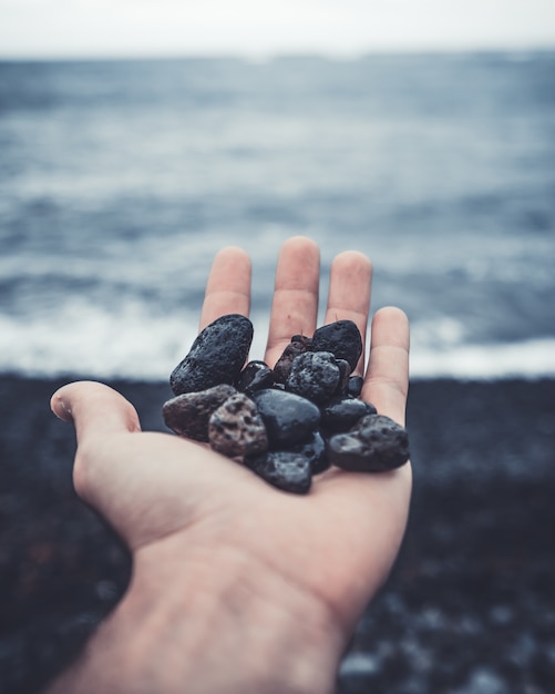 Free photo vertical closeup shot of black stones in the palm of a human