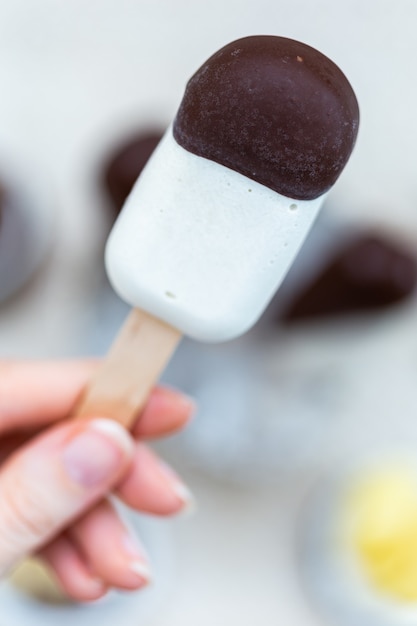 Vertical closeup shot of a female hand holding a raw vegan ice-cream on stick