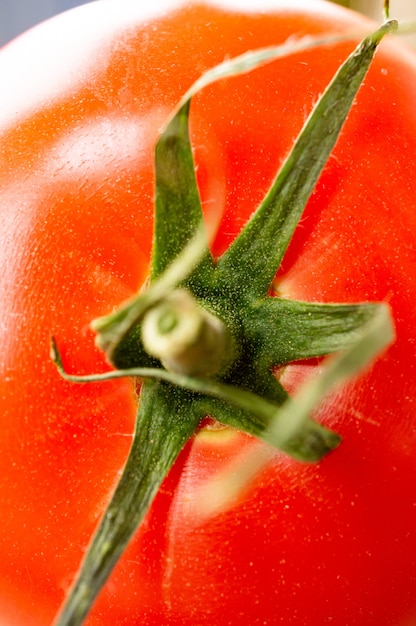 Vertical closeup shot of a fresh raw tomato with its green leaf