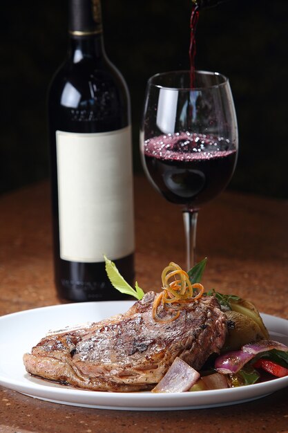 Free Photo vertical closeup shot of a freshly grilled t-bone steak and a glass of wine  in the background