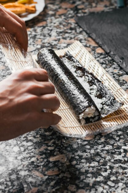 Vertical closeup shot of a process of making a sushi roll on a marble table