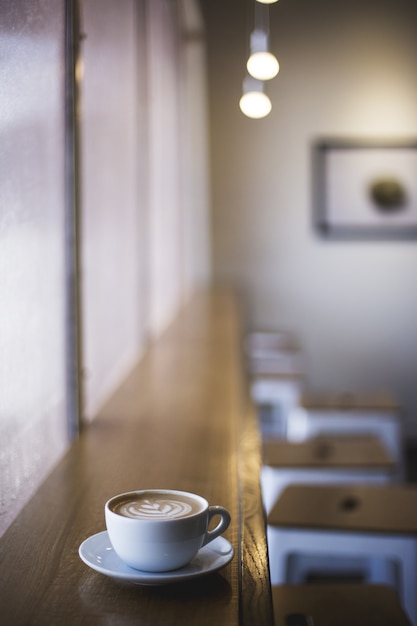 Free photo vertical closeup shot of white cup of latte art coffee on a window shelf in a cafe