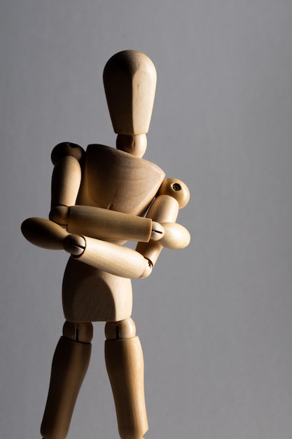 Free Photo vertical closeup shot of a wooden pose doll with crossed arms standing in the shade