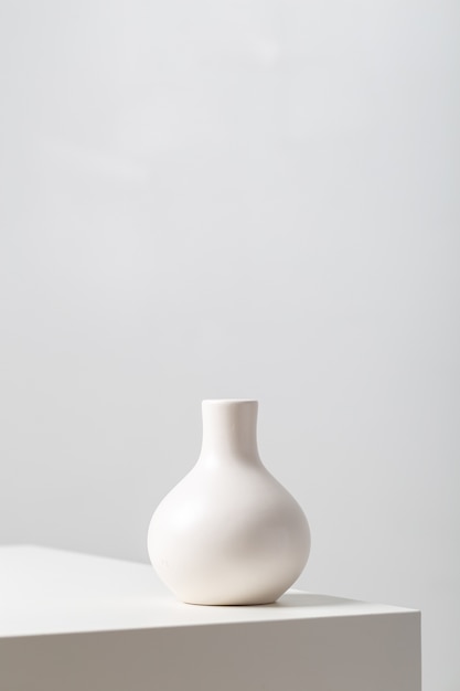 Vertical closeup of a white clay vase on the table under the lights against a white background