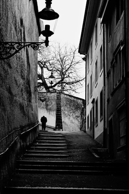 Vertical grayscale shot of a staircase between two buildings leading to upwards