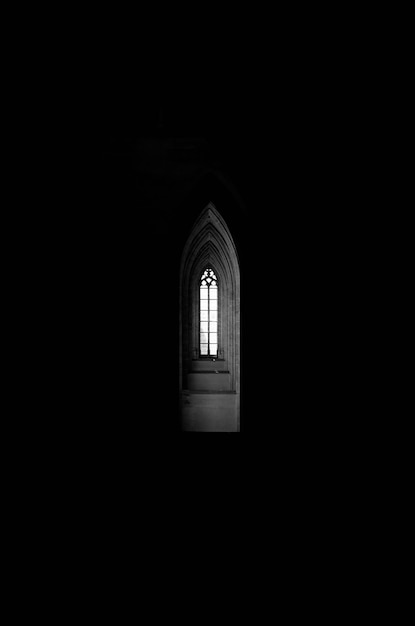 Free photo vertical grey scale shot of a window at the end of an arch shaped hallway in a dark building