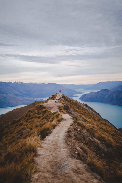 Free photo vertical high angle shot of a person standing on the end of walking road on roys peak in new zealand