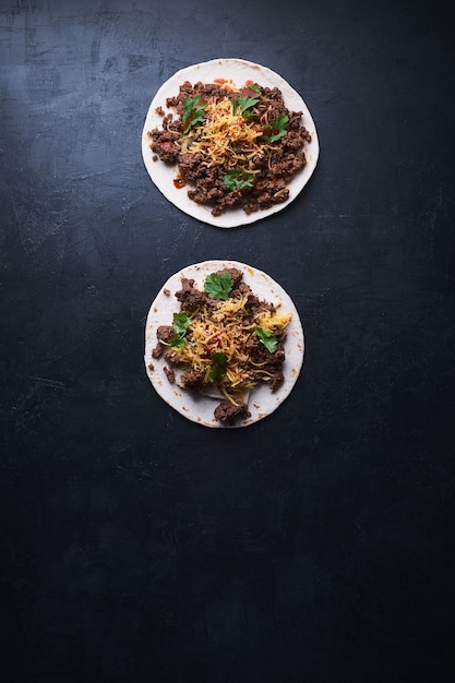 Vertical high angle shot of two tortilla bread with meat and melting cheese on a black surface