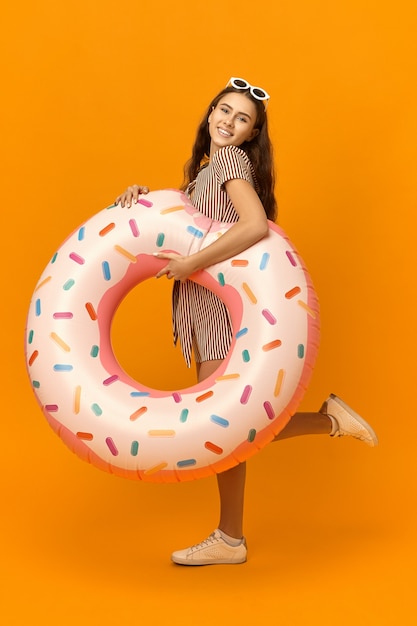 Free Photo vertical image of cheerful pretty girl going to beach carrying rubber circle.