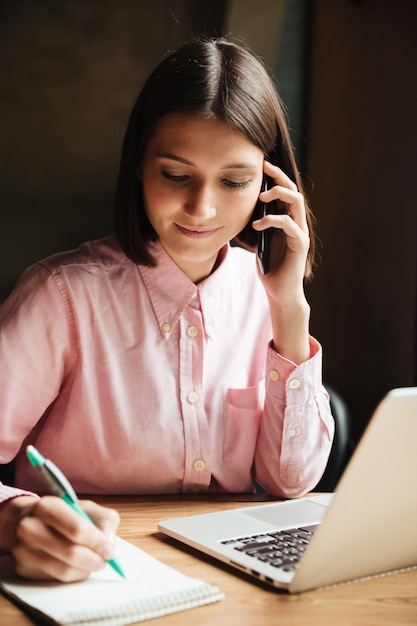 Vertical image of smiling brunette woman sitting by the table