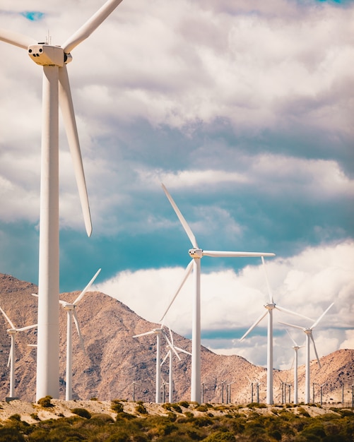 Free Photo vertical low angle shot of a lot of windmills in a field surrounded by high rocky mountains