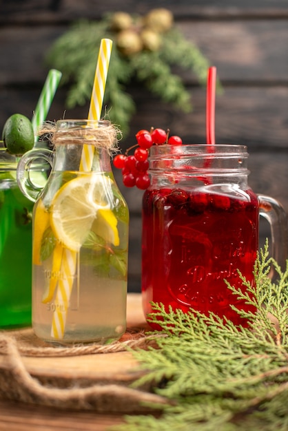 Vertical of organic fuit juices in bottles served with tubes on a wooden cutting board on a brown table