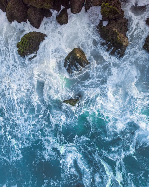 Free photo vertical overhead aerial shot of a wavy blue sea against the rocks