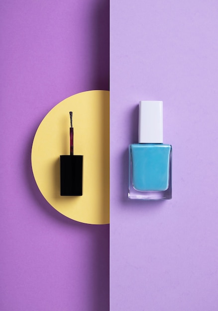 Vertical overhead shot of blue nail polish and a black applicator geometric yellow purple background