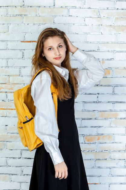 Vertical photo of an adorable student holding her hand to her hair and looking at the camera High quality photo