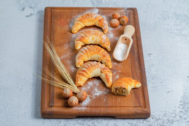 Vertical photo of fresh homemade croissants on wooden board over grey surface.