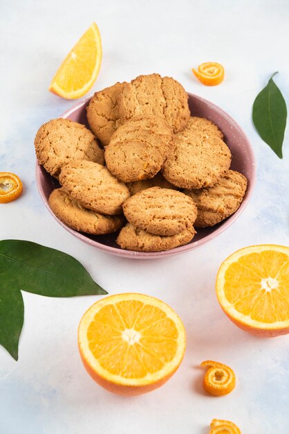 Vertical photo of pile of cookies in bowl and half cut oranges. 