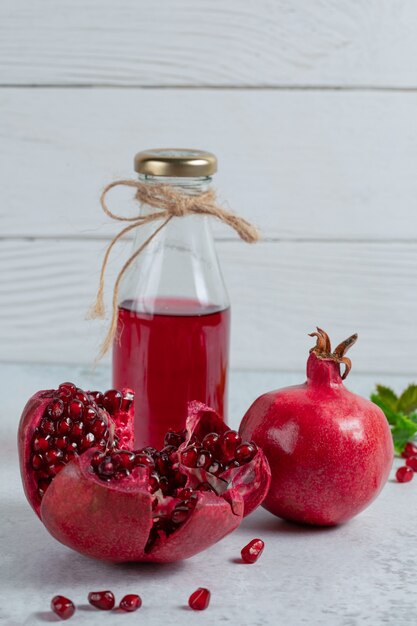 Vertical photo of Sliced or whole pomegranates with bottle of juice.