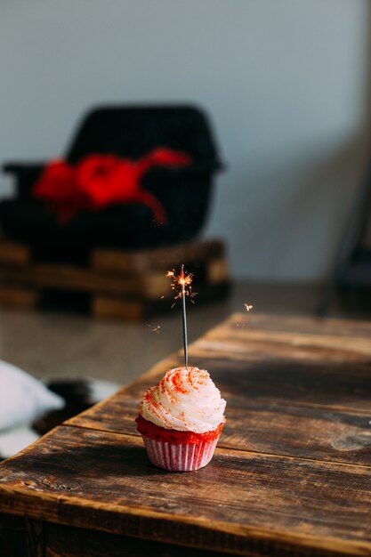 Vertical photo for smartphone screensaver of red velvet pink cupcake, with sparkler candle, decorated with frosting and sugar