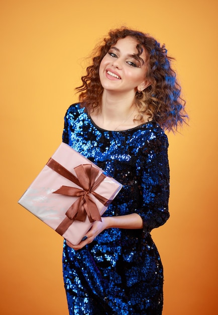 Vertical photo of young lady holding present box and wearing gilded dress High quality photo