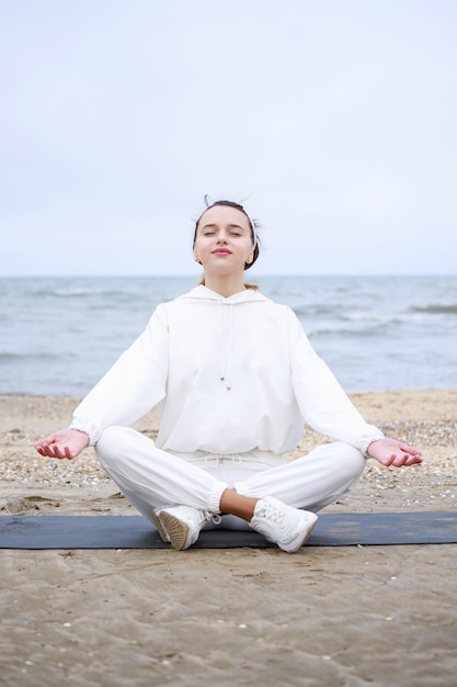 Vertical photo of young lady sittin on mat and doing meditation at the beach High quality photo