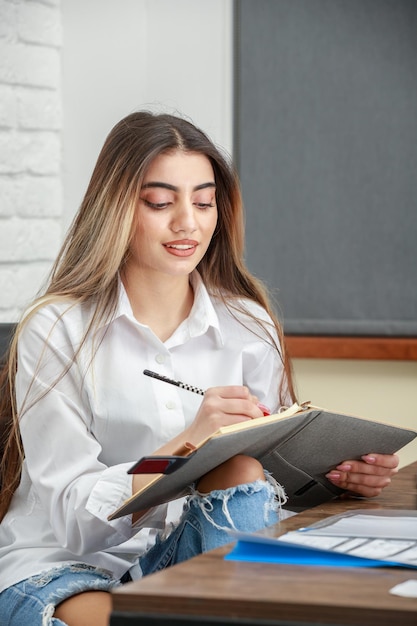 Vertical photo of young lady taking notes while sitting at the office High quality photo