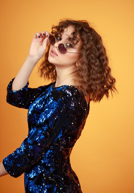 Vertical photo of young wearing sunglasses and gilded dress on orange background High quality photo