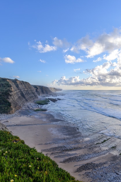 Free photo vertical picture of the beach surrounded by the sea and cliffs under the sunlight and a cloudy sky