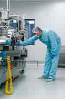 Free photo vertical picture of bended caucasian scientist in blue lab suit trying to fix manufacture machine with shafts in clean factory