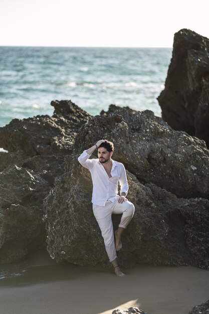 Vertical picture of a brunette male leaning on the rock and posing