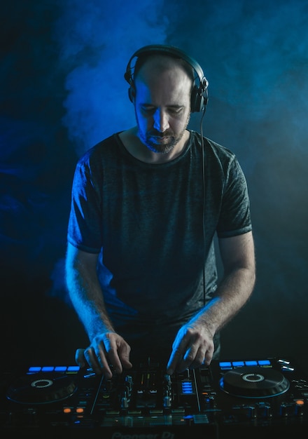 Vertical picture of a male DJ working under the lights against a dark