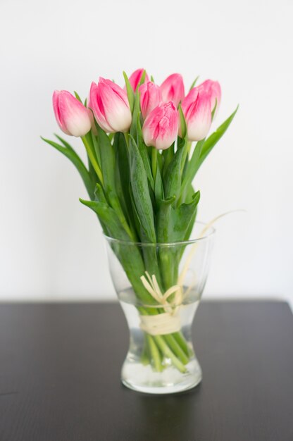 Vertical picture of tulips in a vase on the table under the lights