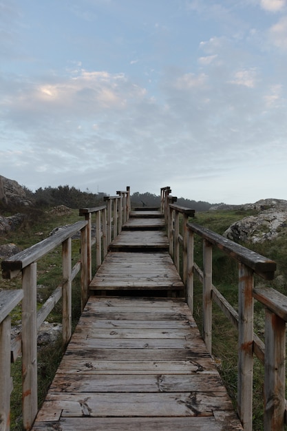 Free Photo vertical picture of wooden steps in a field surrounded by greenery and hills under a cloudy sky