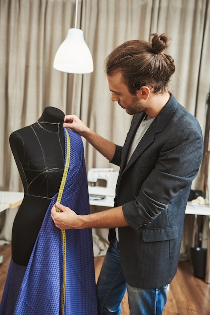 Free Photo vertical portrait of adult good-looking caucasian male fashion designer with stylish hairstyle in fashionable outfit in his studio working on new dress for winter clothes collection