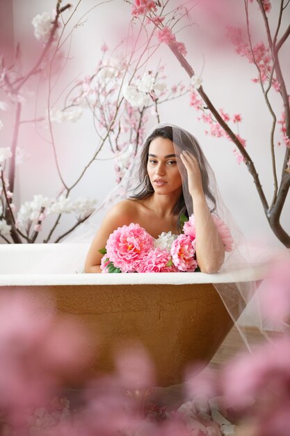 Free photo vertical portrait of young hot model sittin in a bath tube around flowers high quality photo