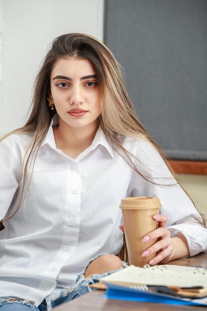 Vertical portrait of young lady holding cup of coffee and looking at the camera