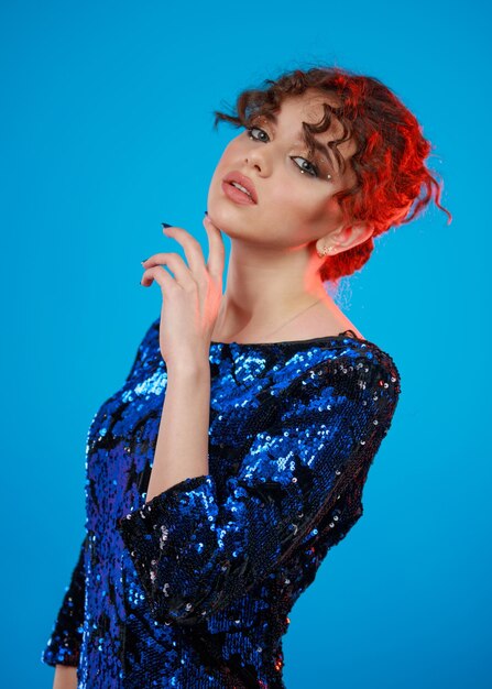 Vertical portrait of young lady put her hand to her chin and looking at the camera on blue background High quality photo