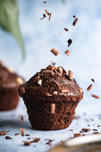 Vertical selective focus shot of chocolate cupcakes on a blue surface with chocolate chips falling