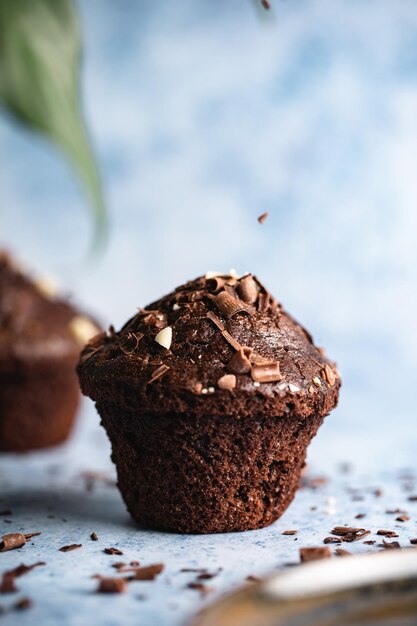 Vertical selective focus shot of chocolate cupcakes on a blue surface with chocolate chips falling