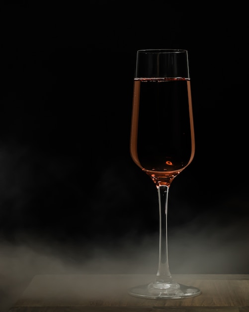 Vertical selective focus shot of a glass of champagne on a wooden surface and a black distance