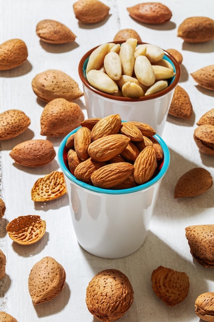 Vertical shot of almonds in cups and scattered on a white surface