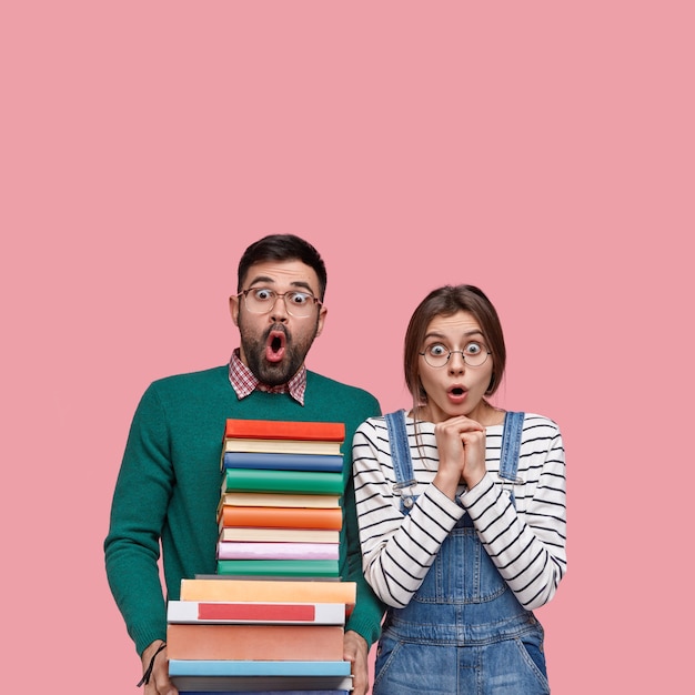 Free photo vertical shot of astonished hipster and girlfriend have deadline task, open mouthes with astonishment, stand closely, read scientific literature