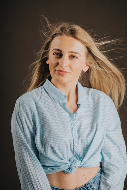 Vertical shot of an attractive blonde female in jeans and a short shirt posing on a brown background