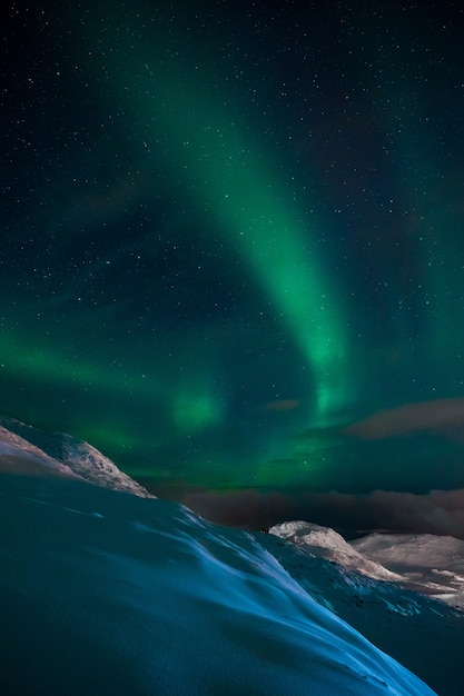 Free photo vertical shot of an aurora in the sky above the hills and mountains covered with snow in norway