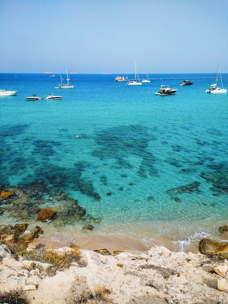 Vertical shot of the beach next to Ibiza and boats in it