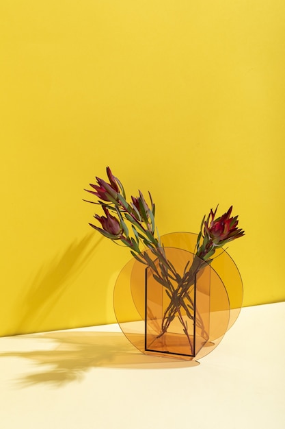 Vertical shot of beautiful red billbergia flowers in a glass vase against a yellow wall