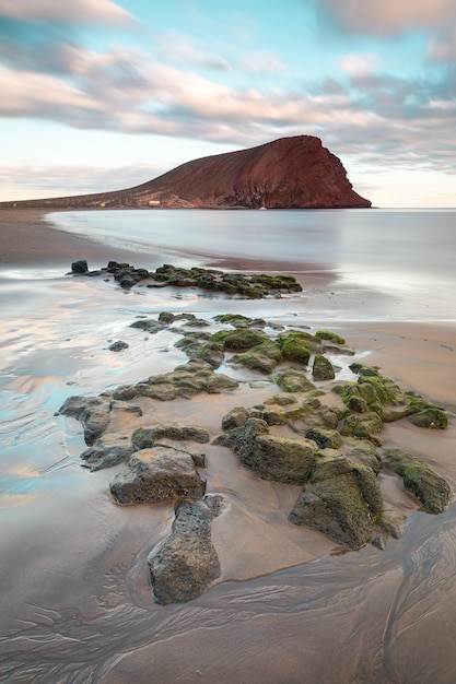 Vertical shot of beautiful sea with a large rock in the background under the cloudy sky