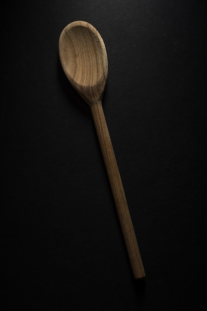 Free photo vertical shot of a big wooden spoon isolated on black background