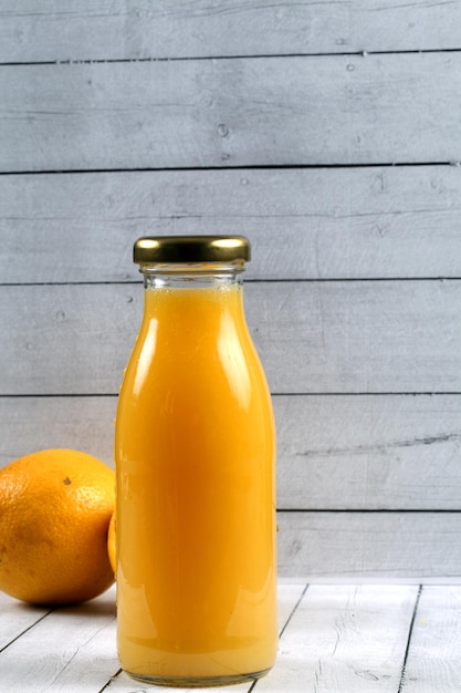 Free Photo vertical shot of a bottle of fresh orange juice and oranges on a wooden surface